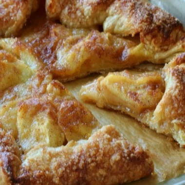 Slice of delicious rustic French apple tart with fresh apples on a wooden table