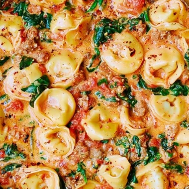 Creamy tortellini in a bowl with sausage, spinach, and tomatoes topped with mozzarella