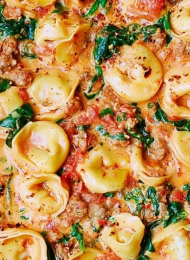 Creamy tortellini in a bowl with sausage, spinach, and tomatoes topped with mozzarella
