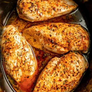 Slow cooker chicken breasts served on a plate, garnished with herbs.