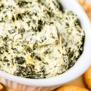 Easy hot spinach dip served in a bowl with chips and veggies.