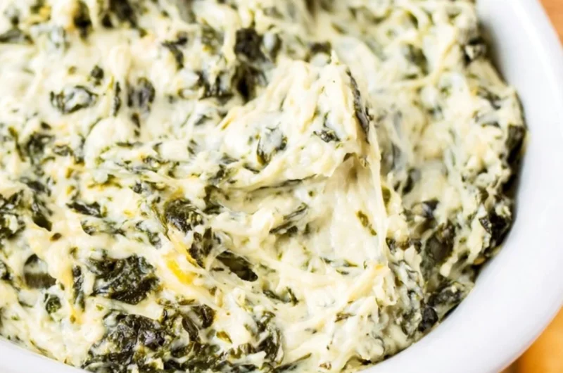 Easy hot spinach dip served in a bowl with chips and veggies.