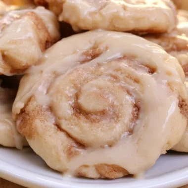 Delicious soft cinnamon roll cookies topped with icing on a wooden table.