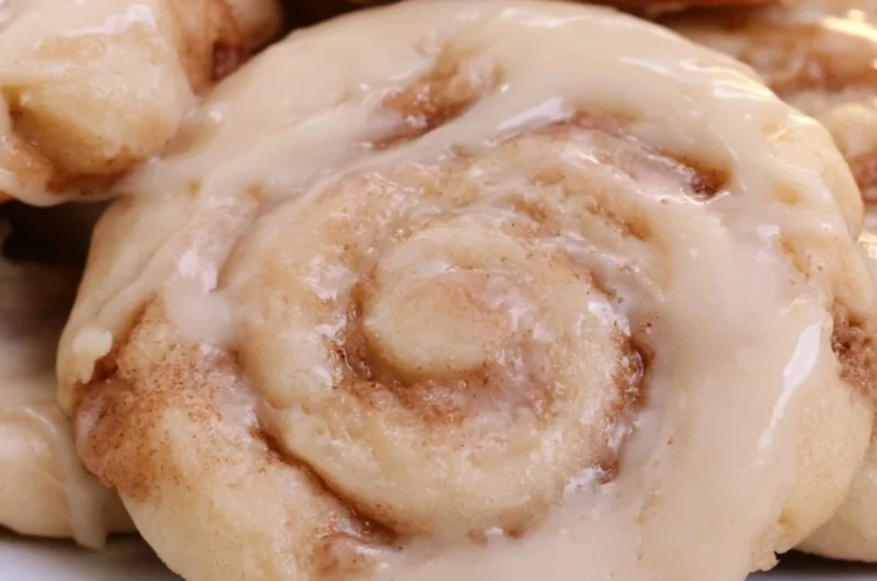 Delicious soft cinnamon roll cookies topped with icing on a wooden table.